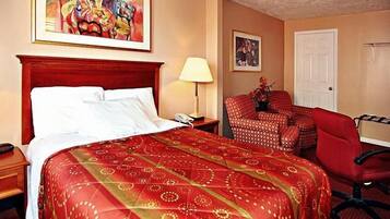 Habitación de hotel con cama, escritorio, silla, lámpara y dos cuadros en la pared.