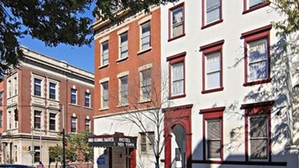 A multi-story building with a red and white facade, a visible storefront with signage, and parked cars along the street. - Midtown inn (Baltimore)