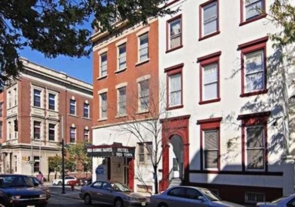 A multi-story building with a red and white facade, a visible storefront with signage, and parked cars along the street. - Midtown inn (Baltimore)