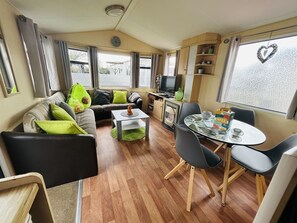 Ein gemütlicher Wohnbereich mit einer Couch, einem Couchtisch, einem Fernseher und einem Esstisch mit Stühlen.