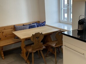 Eine hölzerne Bank, ein Holztisch und zwei Holzstühle in einem Raum mit einem Fenster.