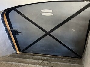 A closed, dark-colored door with a metal handle and a cross-shaped design on the glass. - Plaz 117, (Ftan) by Interhome (Ftan)