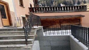 A set of concrete steps leading to a wooden door, with a metal railing on the upper landing.