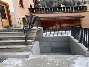 A set of concrete steps leading to a wooden door, with a metal railing on the upper landing.