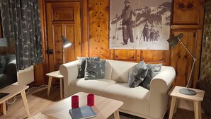 A cozy living room with a wooden paneled wall, a large framed picture, a white sofa, and a coffee table with books and red cups.