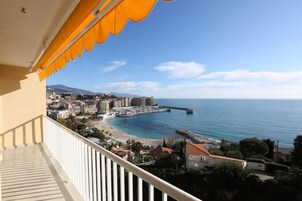 Un balcón con vistas a una ciudad costera, que incluye edificios, una playa y un muelle.