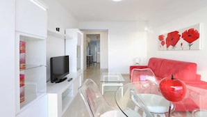 Ein modernes Wohnzimmer mit Fernseher, Glastisch und einem roten Sofa.