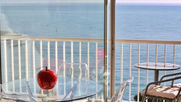 Ein Balkon mit einem Glastisch, einem roten Apfel und Blick aufs Meer.
