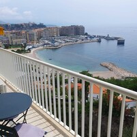 Un balcón con vistas a un puerto deportivo, una playa y el horizonte de la ciudad.