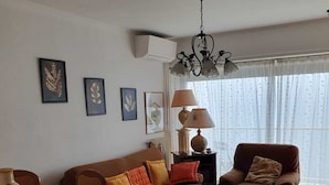 Ein Wohnzimmer mit braunem Sofa, einem Couchtisch, einem Esstisch mit Blumenmuster und einer Lampe.