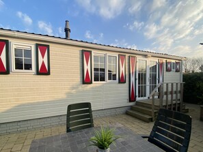 A mobile home with a brick foundation, a covered porch, and a small outdoor seating area with a table and chairs. - RBR 813 - Beach Resort Kamperland by Interhome (Kamperland)