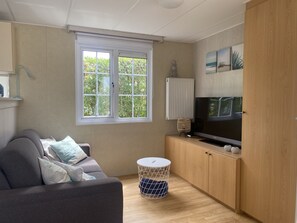 A modern living room with a sofa, a television, a radiator, and a window with a view of greenery. - RBR 813 - Beach Resort Kamperland by Interhome (Kamperland)