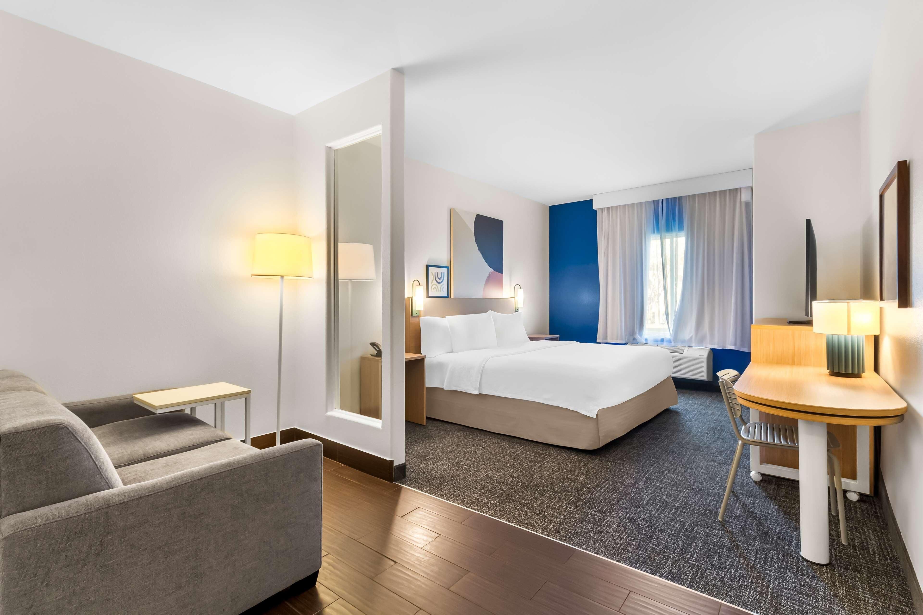 Ein Hotelzimmer mit Bett, Schreibtisch, Sessel, Sofa und Lampe.