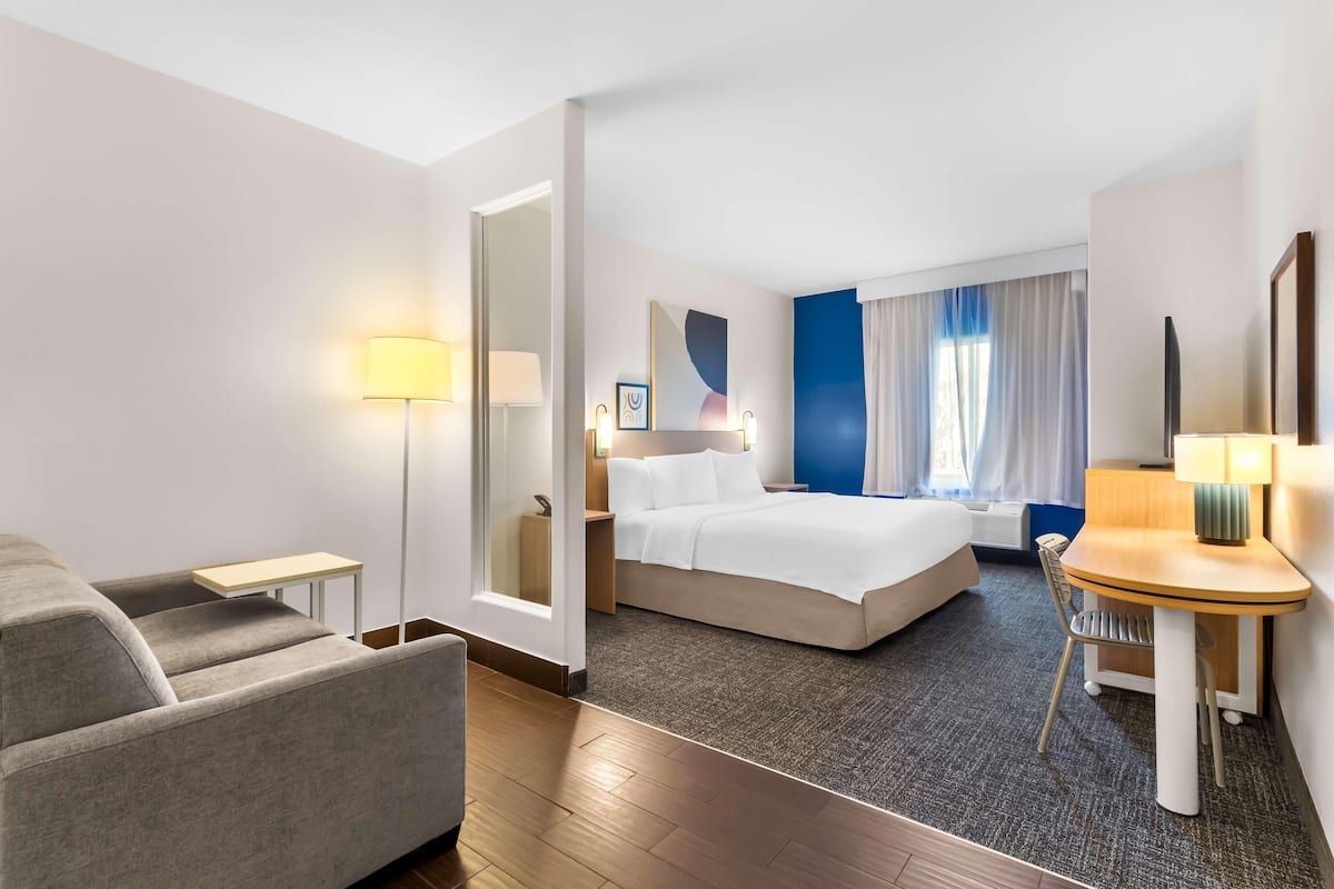 Ein Hotelzimmer mit Bett, Schreibtisch, Sessel, Sofa und Lampe.