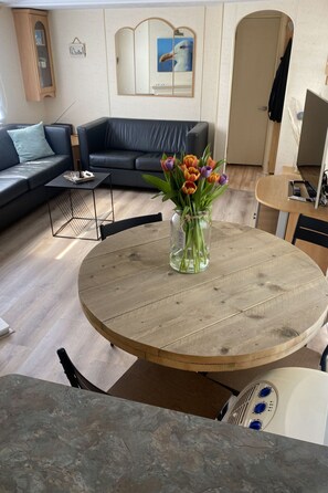 A living room with a round wooden table, a black leather sofa, a glass coffee table, and a vase of tulips. - RBR 232 - Beach Resort Kamperland by Interhome (Kamperland)