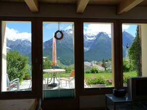 Una stanza con ampie finestre che offrono vista sulle montagne, un tavolo con sedie e una televisione.