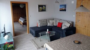 Een woonkamer met een bank, een ronde glazen tafel, een houten deur en een plafond met zichtbare balken.