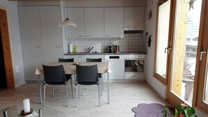 Een moderne keuken met witte kasten, een eethoek met een glazen tafel, en uitzicht door een groot raam.