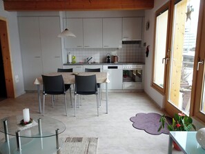 Una cucina moderna con mobili bianchi, un'area pranzo con tavolo in vetro e vista attraverso un'ampia finestra.