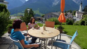 Een ronde tafel met stoelen en een oranje parasol in een pittoreske buitenomgeving, met bergen op de achtergrond.