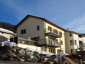 A multi-story building with balconies, a stone wall in front, and a clear sky. - Chasa Fionas - Einfamilienhaus Fam. Pitsch, (Ftan) by Interhome (Ftan)