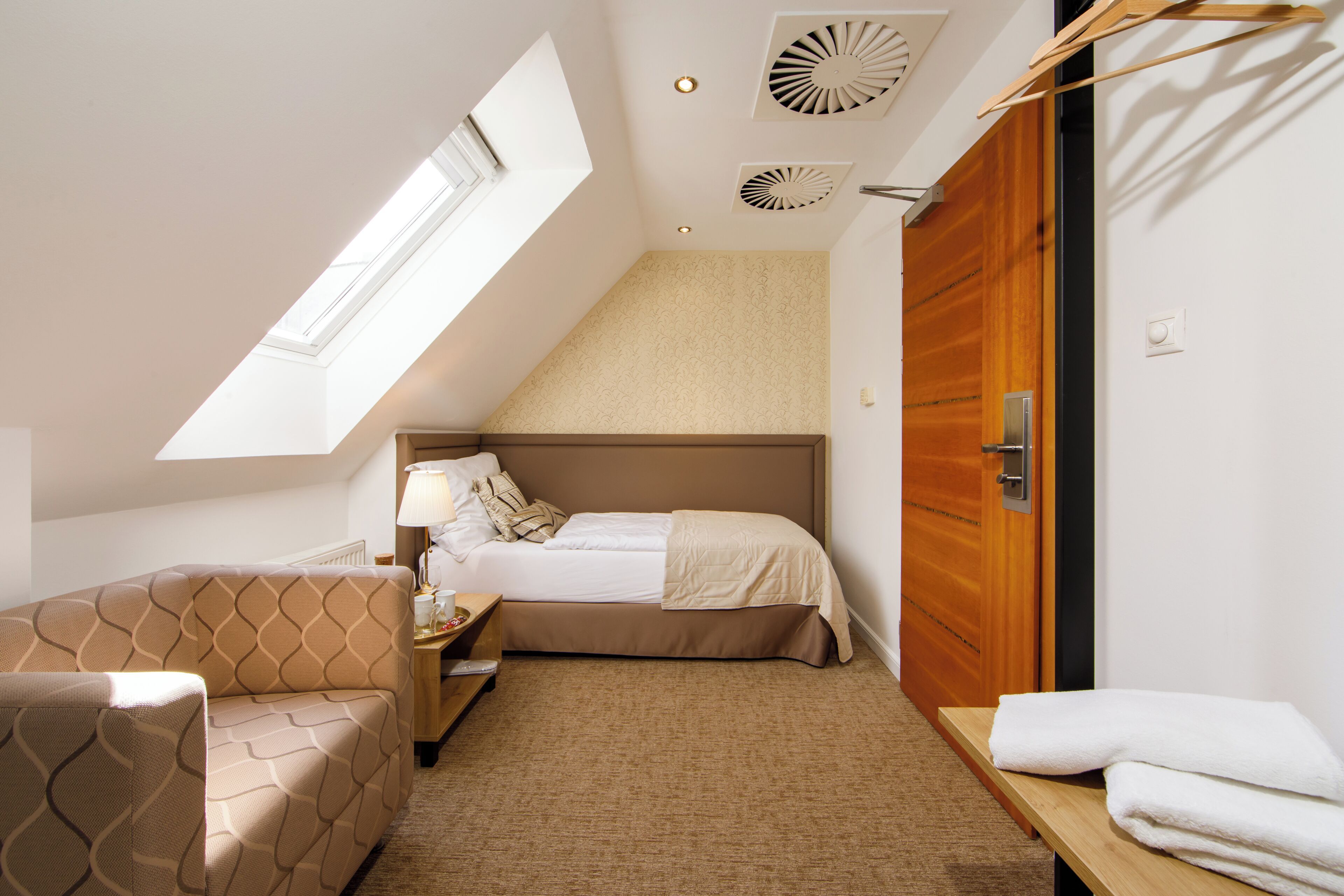 Een slaapkamer met een bed, een slaapbank, een nachtkastje, een lamp, een raam en een houten deur.