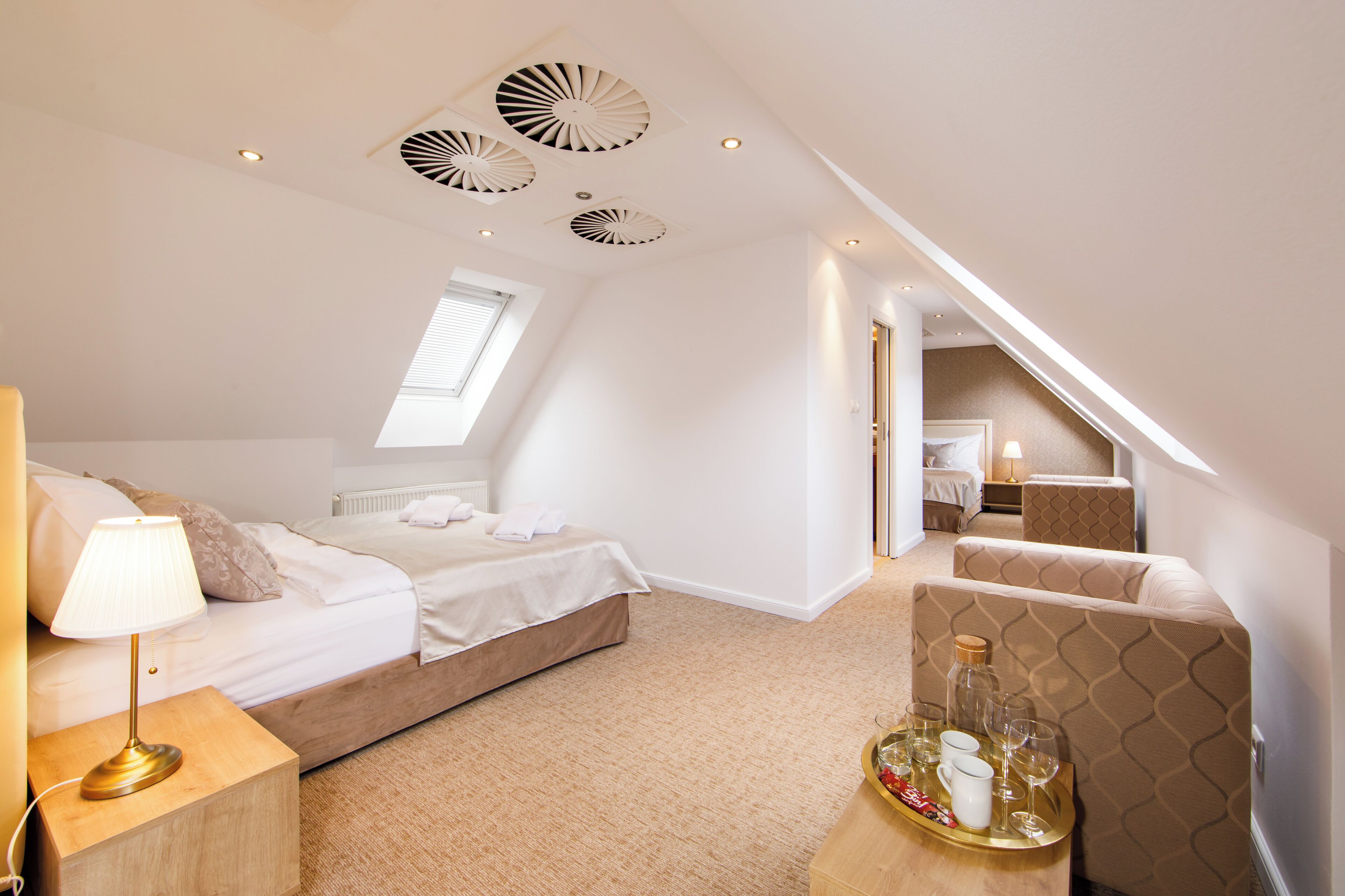 Een slaapkamer met twee bedden, een nachtkastje met een lamp, een dienblad met glazen en een fles, en een zithoek met een tafel en stoelen.