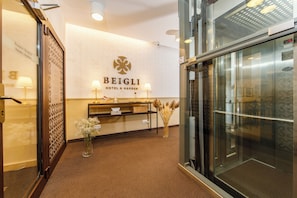 A reception area with a reception desk, a wall-mounted sign reading 'BEIGLI HOTEL & GARDEN,' and an elevator.