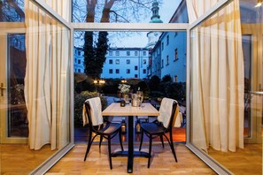 Un comedor con mesa y sillas, vista a edificios y un separador de vidrio.