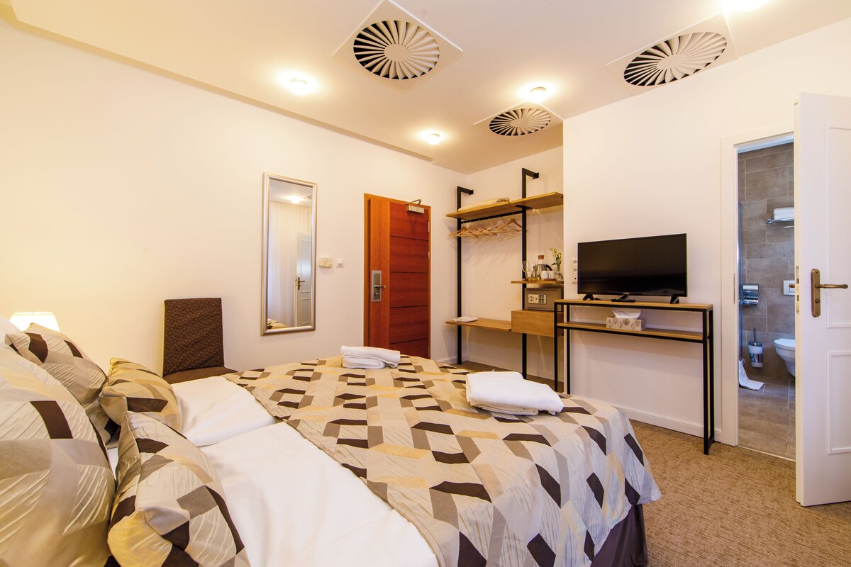 Habitación de hotel con cama, televisor, escritorio y baño visible a través de una puerta abierta.