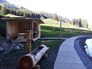 A wooden cabin with a deck, a log, and a small outdoor seating area. - Chasa Cumulus/DG Ferienwohnung Sainas 139 A, (Ftan) by Interhome (Ftan)