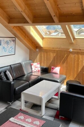 A loft-style room with a wooden ceiling, a black leather sofa, a white coffee table, and a skylight. - Chasa Cumulus/DG Ferienwohnung Sainas 139 A, (Ftan) by Interhome (Ftan)