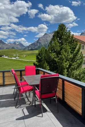Eine Terrasse mit Tisch und Stühlen mit Blick auf eine gebirgige Landschaft.