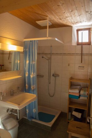 Et badeværelse med brusebad, håndvask, toilet og en hylde med håndklæder.