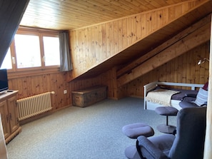 A small, cozy attic bedroom with a sloped ceiling, a single bed, a wooden dresser, a radiator, and a window. - Vichava 8, Süd, (Ftan) by Interhome (Ftan)