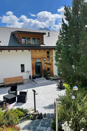 Ein Gebäude mit Holzfassade, einem Kiesweg und Außenbestuhlung.