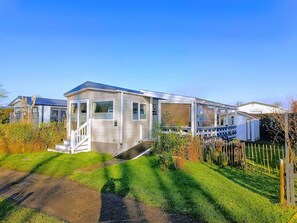 Ein Bungalowmobilheim mit überdachter Veranda, kleinem Vorgarten und blauem Himmel.