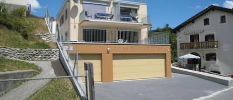 Ein zweistöckiges Gebäude mit Garage, einem Balkon im oberen Geschoss und einer Steintreppe, die zum Eingang führt.