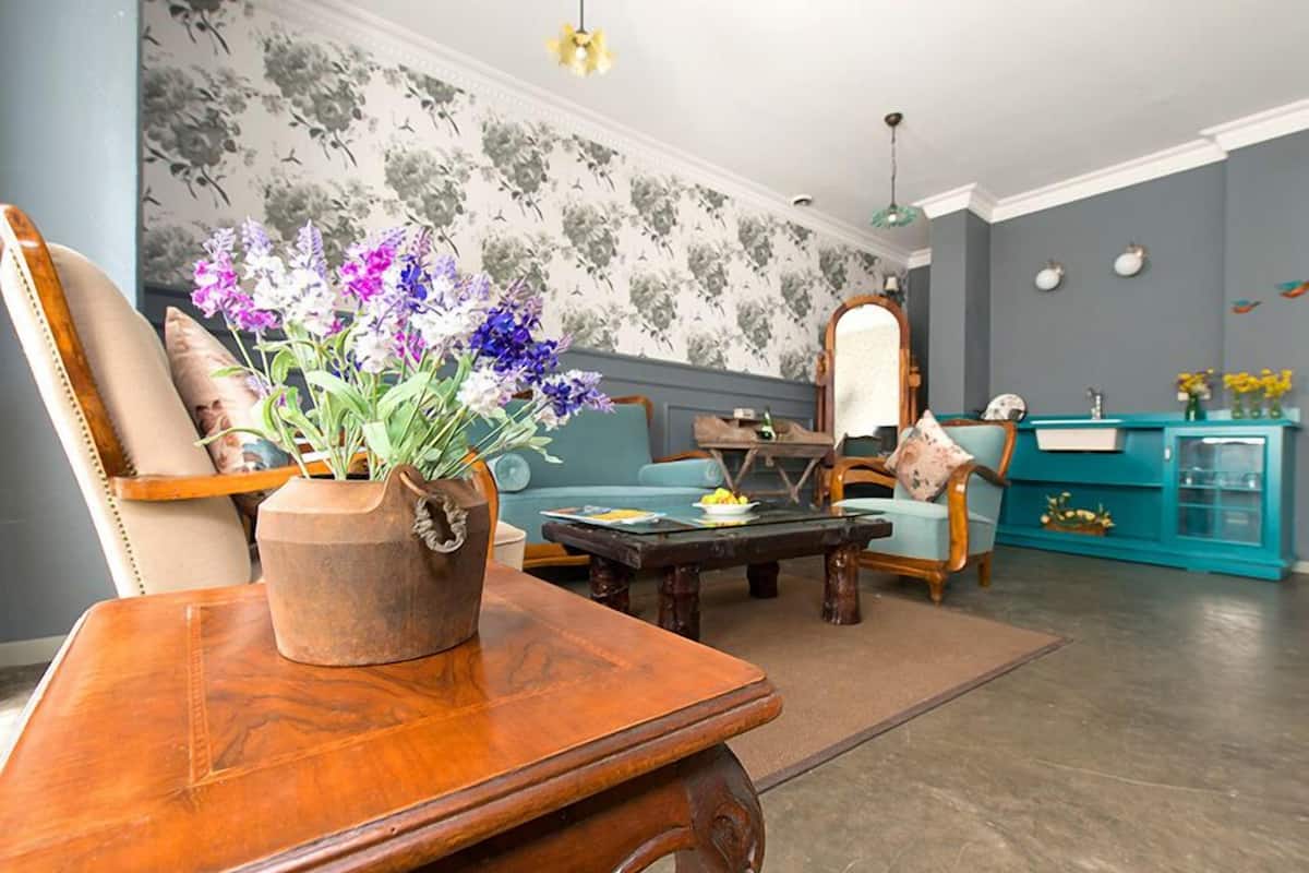 A living room with a wooden coffee table, a sofa, a teal cabinet, and a floral wallpaper.