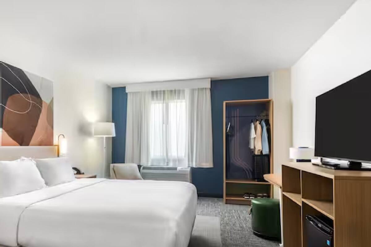 A hotel room with a large bed, bedside tables, a TV, a wardrobe, and a window with curtains.