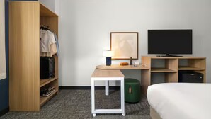 Habitación de hotel con cama, televisor, escritorio con lámpara, armario y una mesita.