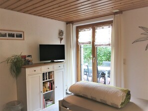 Een kamer met een televisie op een houten kast, een boekenkast, een raam met gordijnen en een plant.