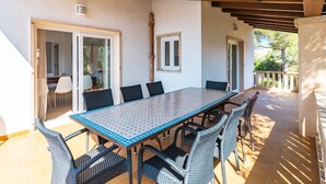 Un patio techado con una larga mesa de comedor y sillas de mimbre, techo de madera y vistas al exterior.