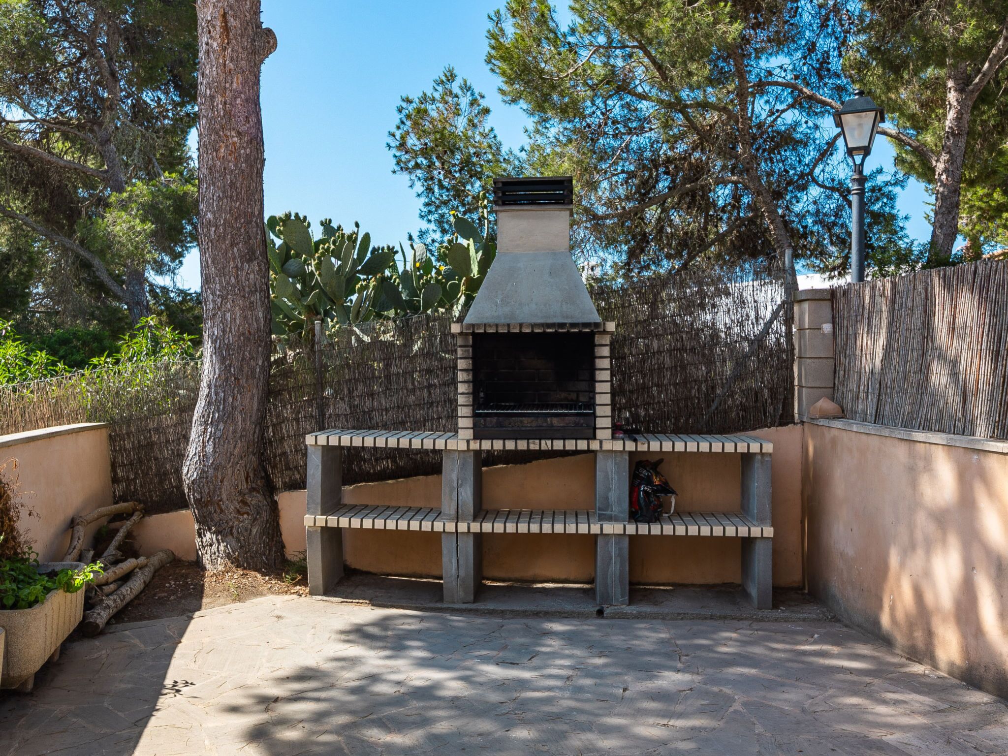 An outdoor brick-built barbecue area with a chimney, surrounded by trees and a fence.
