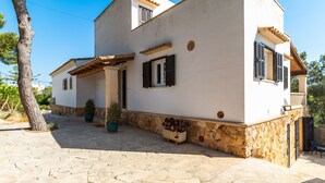 Una casa de dos pisos con base de piedra, un patio con tejas y plantas en macetas.