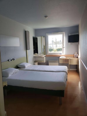 A hotel room with two beds, a desk, a TV, a window, and a bathroom.