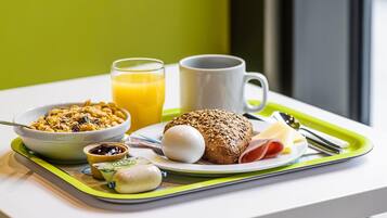 Bandeja de desayuno con cereal, jugo, una taza, un sándwich y un recipiente pequeño de mermelada.