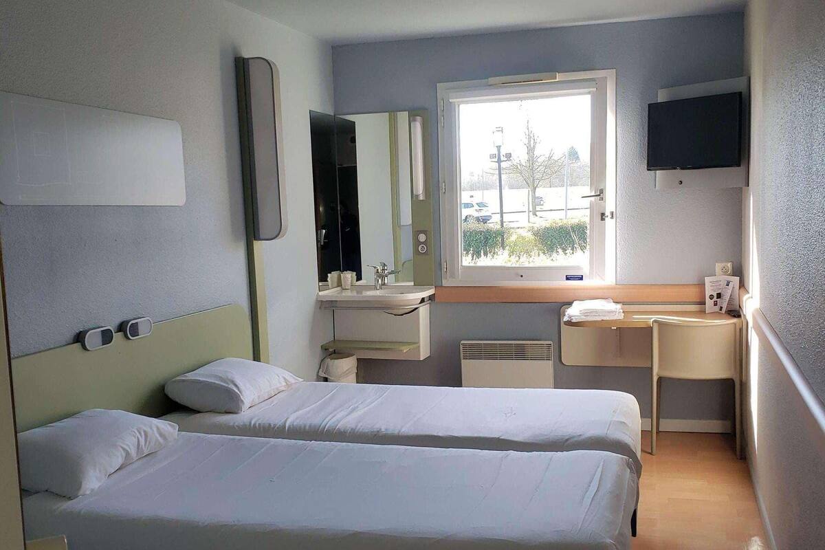 Une chambre d’hôtel avec deux lits, un bureau, une télévision, une fenêtre et une salle de bain.