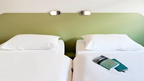 A hotel room with two beds, white bedding, a green accent wall, and a small wall-mounted light fixture. - Ibis Budget Dommartin les Cuiseaux (Dommartin-lès-Cuiseaux)