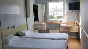 A hotel room with two beds, a window, a desk, a mirror, a TV, and a bathroom. - Ibis Budget Dommartin les Cuiseaux (Dommartin-lès-Cuiseaux)